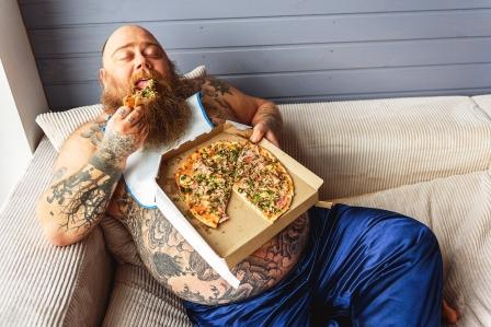 tuk na břichu. tlustý líný muž jí pizzu na gauči